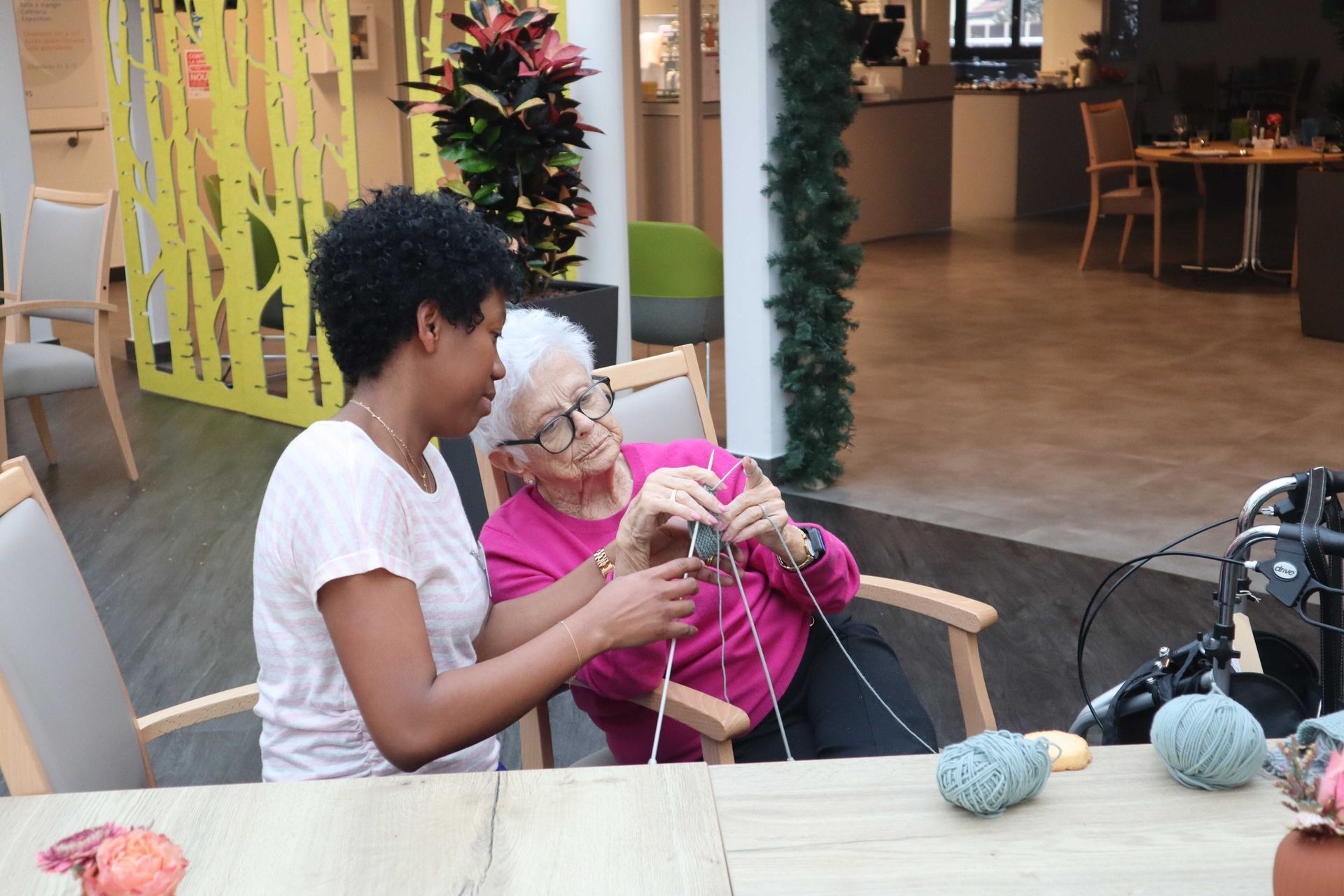 Deux soignantes parlent à une femme âgée assise à une table.
