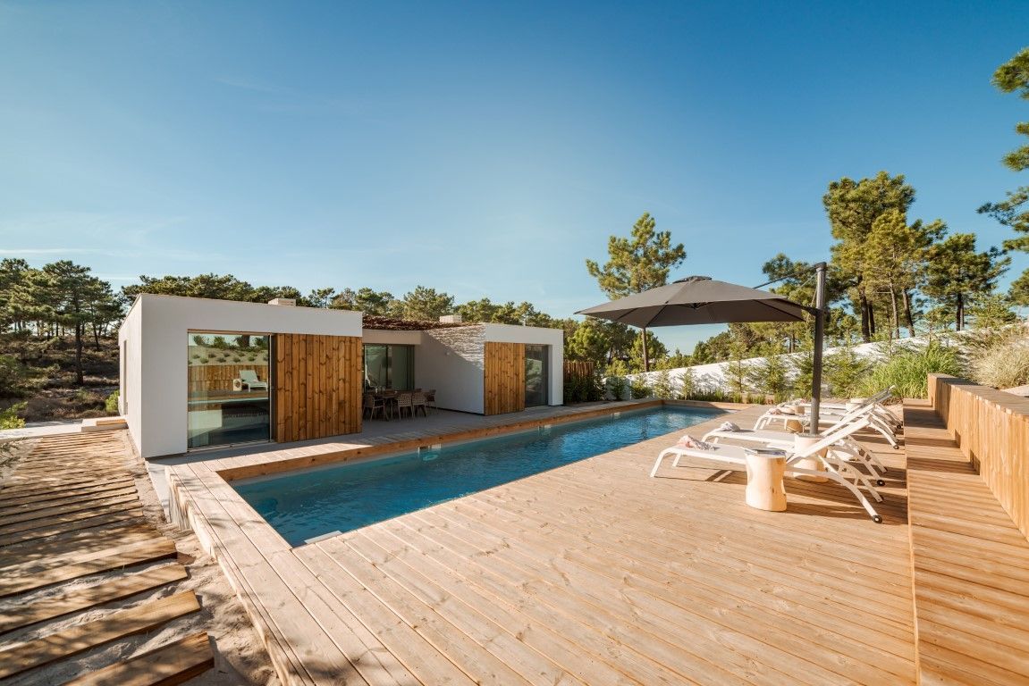 Modern home with rectangular pool, wooden deck, lounge chairs, and umbrella on a sunny day.