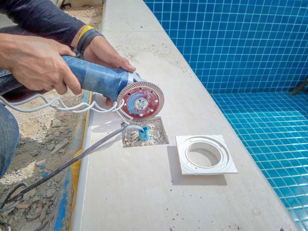 Person using power tool to grind around pool drain. Blue pool tiles in background.
