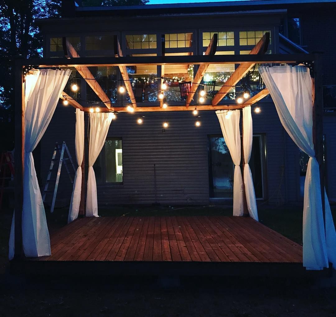 Un gazebo en bois avec des rideaux blancs et des lumières suspendues au plafond