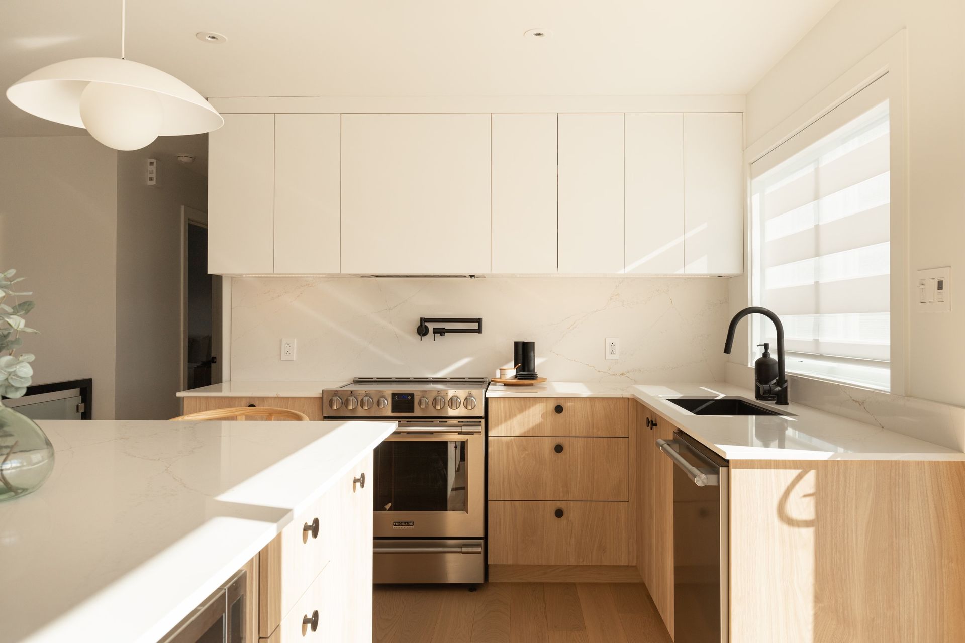 Une cuisine avec des armoires blanches, des appareils en acier inoxydable, un évier et une fenêtre.