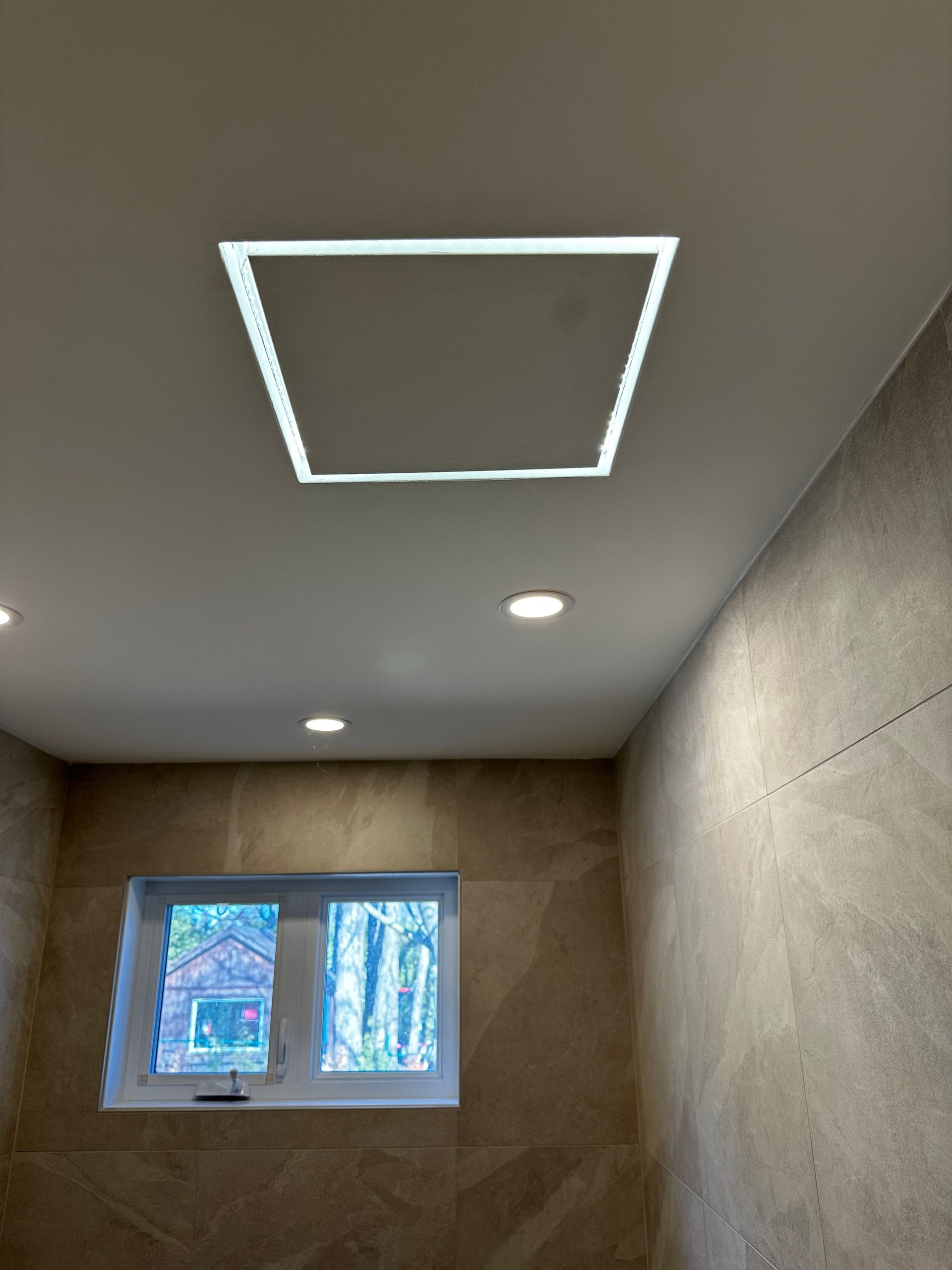 Une salle de bain avec un luminaire carré au plafond et une fenêtre.
