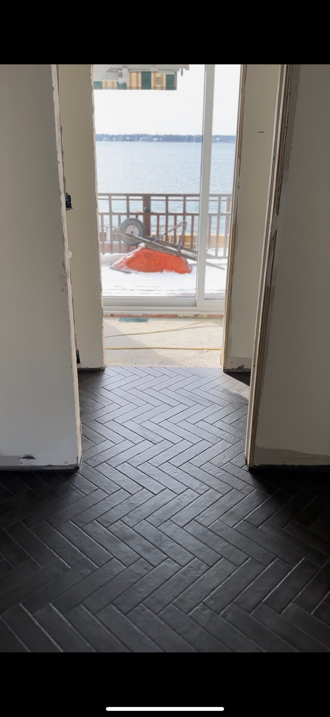 Une pièce avec un sol en carrelage noir et une porte coulissante en verre donnant sur un balcon.