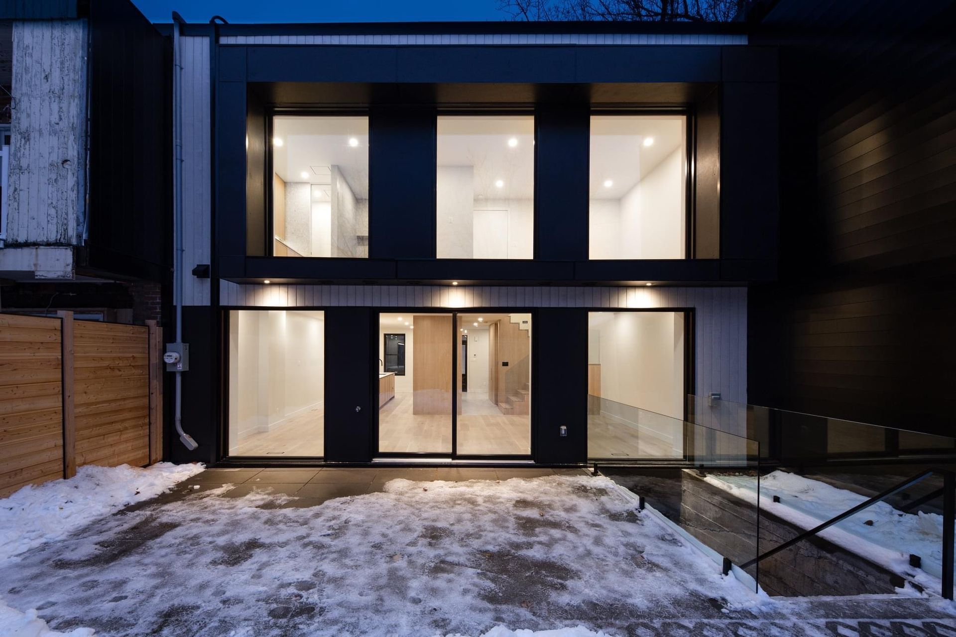 L'arrière d'une maison avec beaucoup de fenêtres et de la neige au sol.