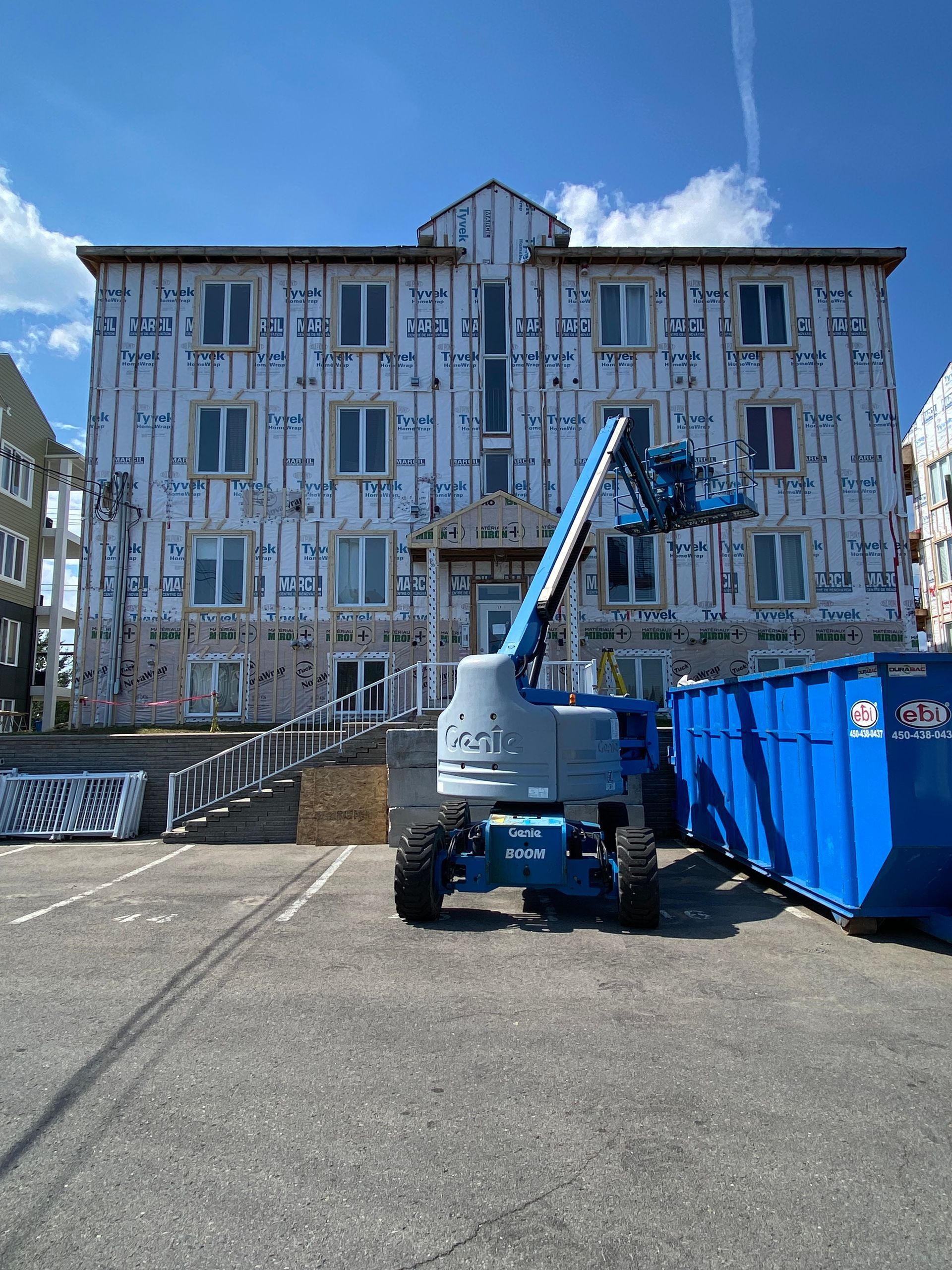 Un grand bâtiment en construction avec une benne bleue devant.