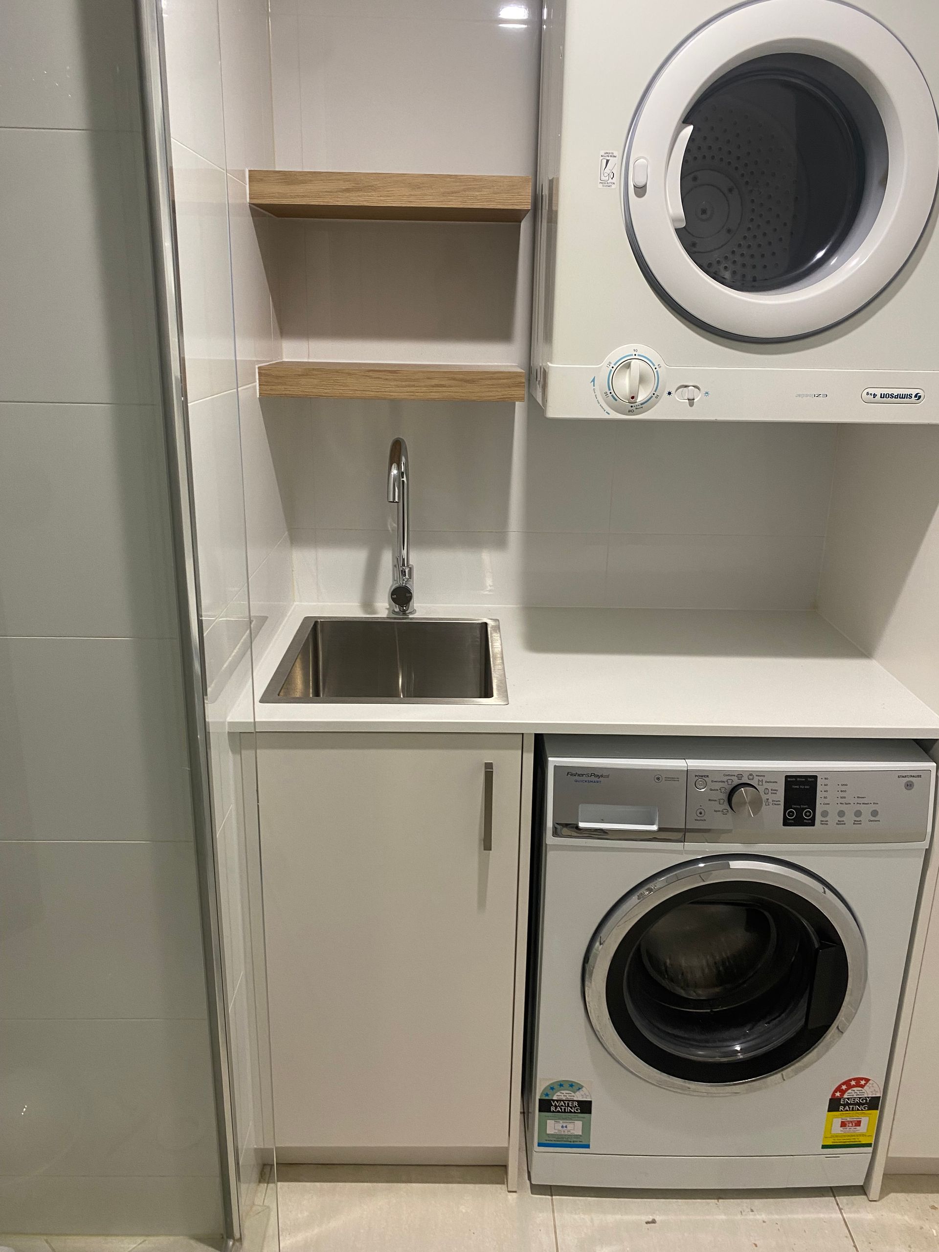 Laundry room with a washer, dryer, sink, and wooden shelves. White cabinets and walls. — Cut N Edge Panel Factory In Coolum Beach, QLD