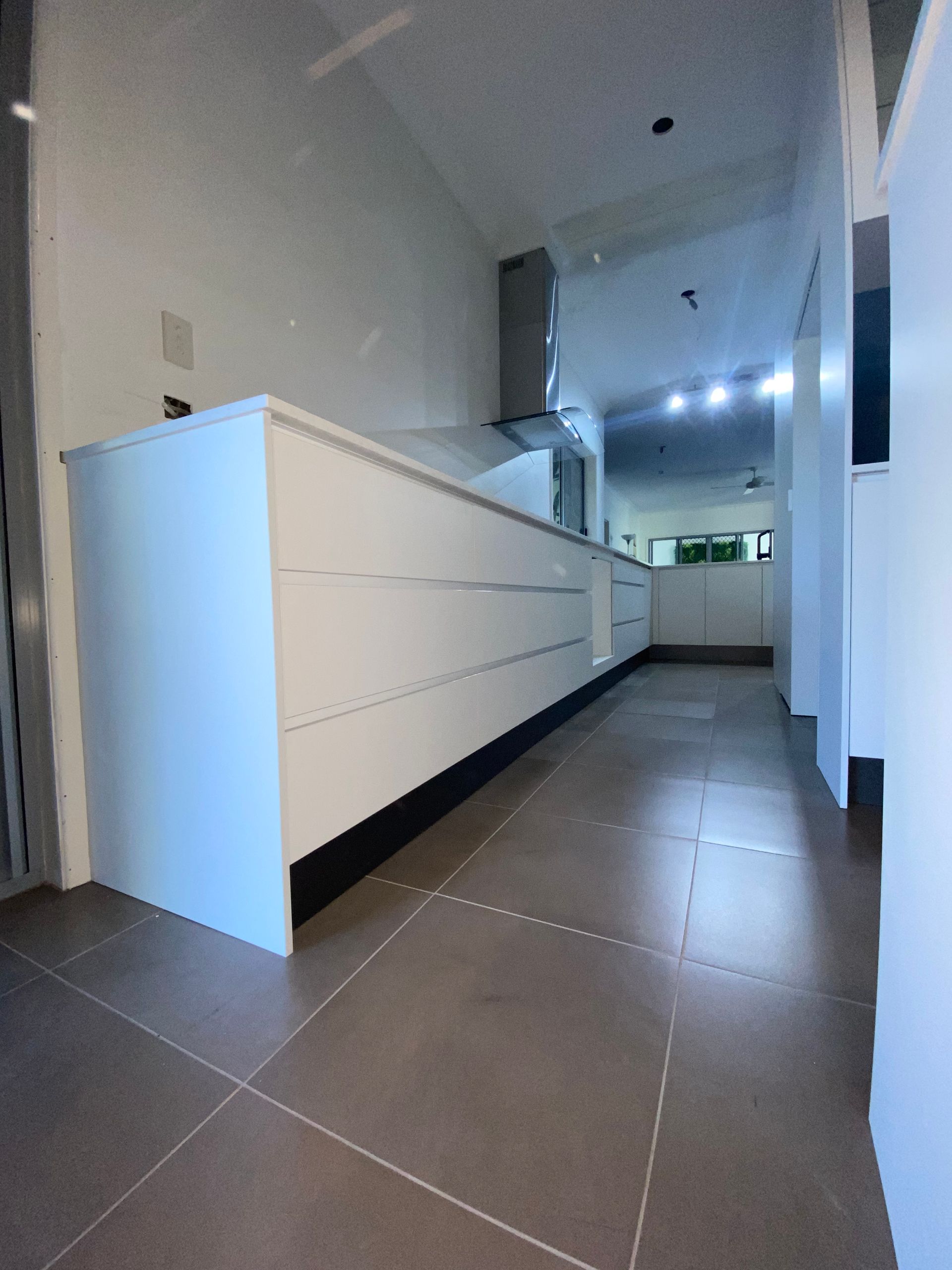 Modern white kitchen with long countertop, cabinets, and dark flooring. — Cut N Edge Panel Factory In Coolum Beach, QLD