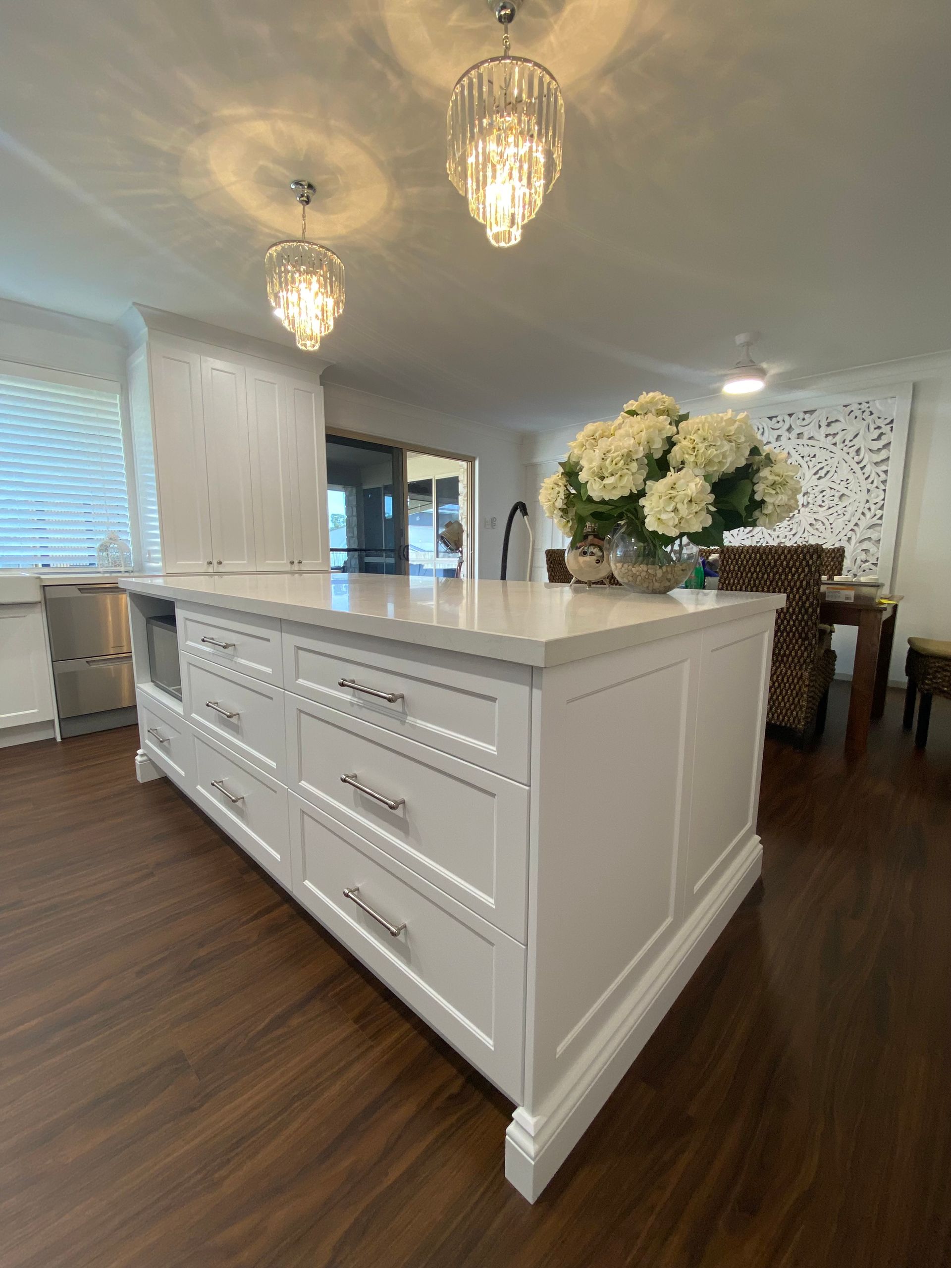 White kitchen island with drawers, marble countertop, flowers, and two hanging lights. — Cut N Edge Panel Factory In Coolum Beach, QLD