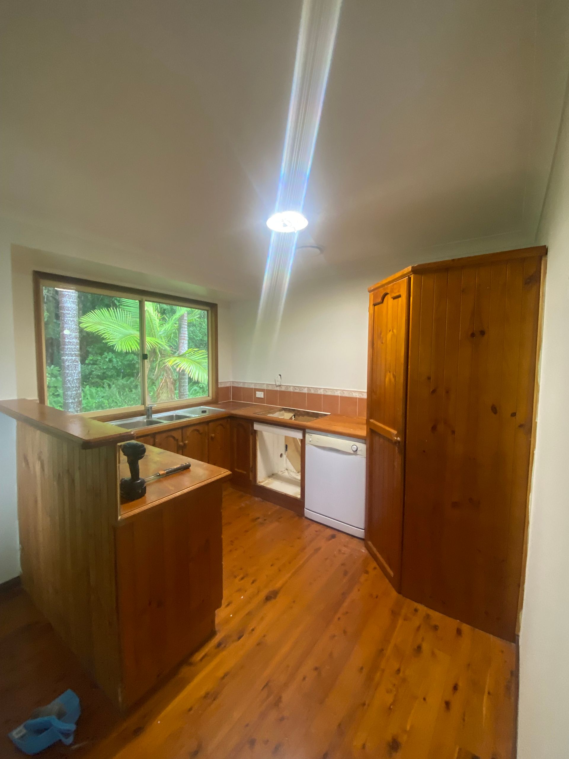 Wooden kitchen with an island, cabinets, and a window overlooking greenery. — Cut N Edge Panel Factory In Coolum Beach, QLD