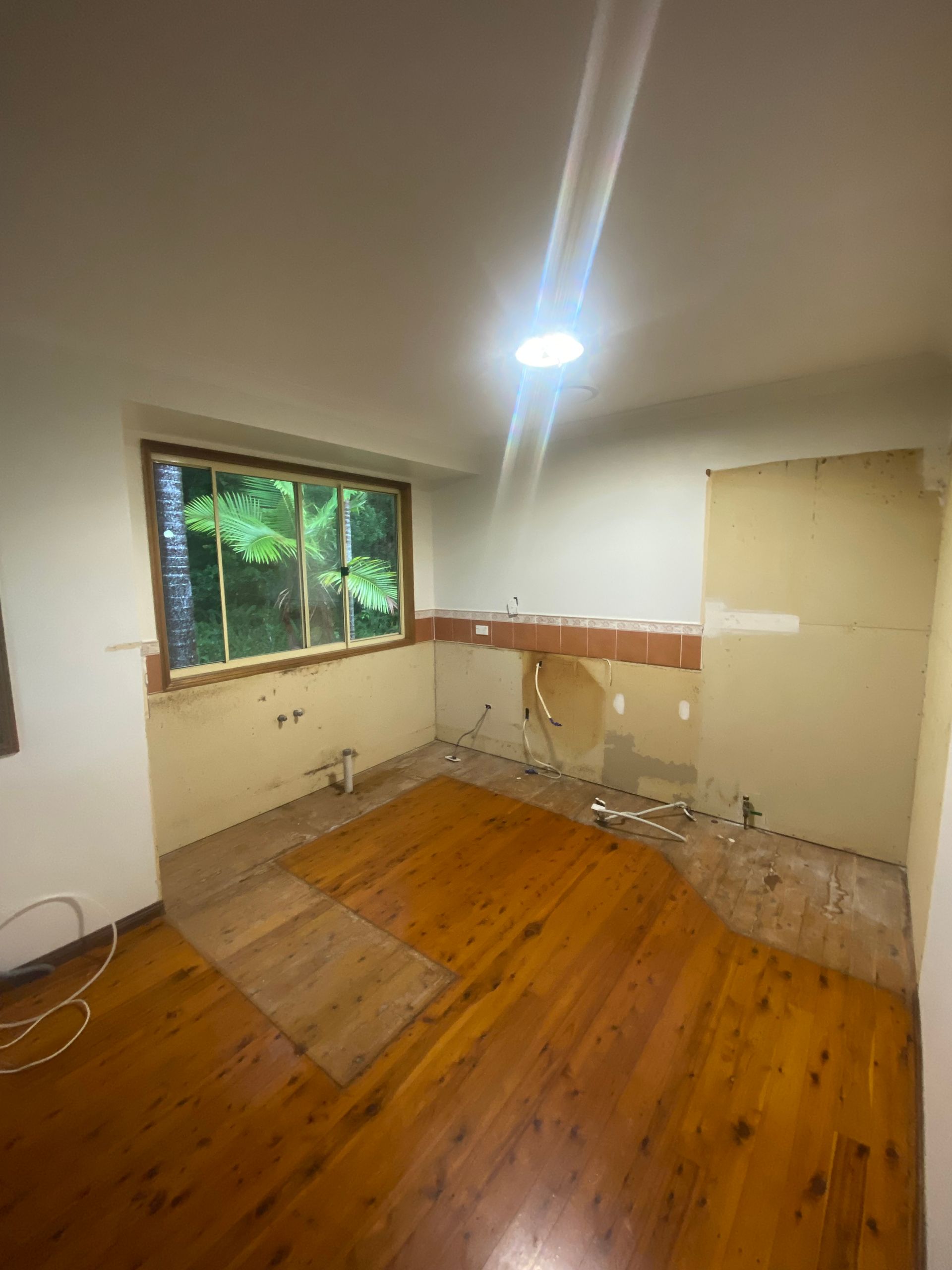 Room under renovation with exposed walls, wood floor, a window, and plumbing. — Cut N Edge Panel Factory In Coolum Beach, QLD