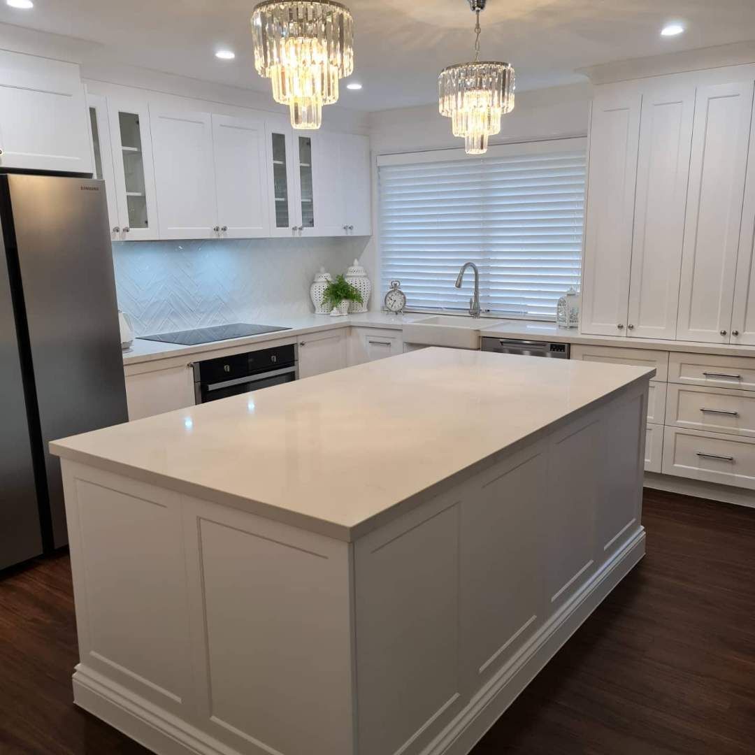White kitchen with island, chandeliers, stainless steel appliances, and wood floors. — Cut N Edge Panel Factory In Coolum Beach, QLD
