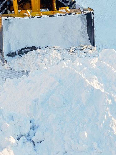 A snowplow pushing a pile of snow on a bright, sunny day.