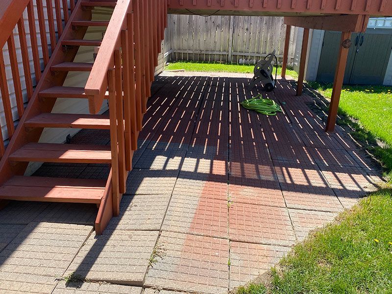Brick patio beneath a deck and stairs, casting shadow stripes in sunlight.