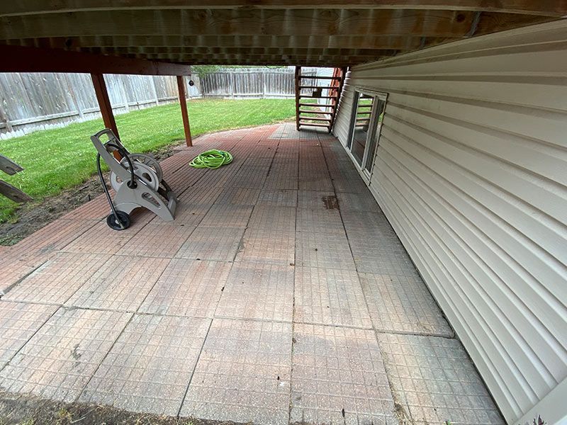 Brick patio under deck next to house. Pressure washer on the left.