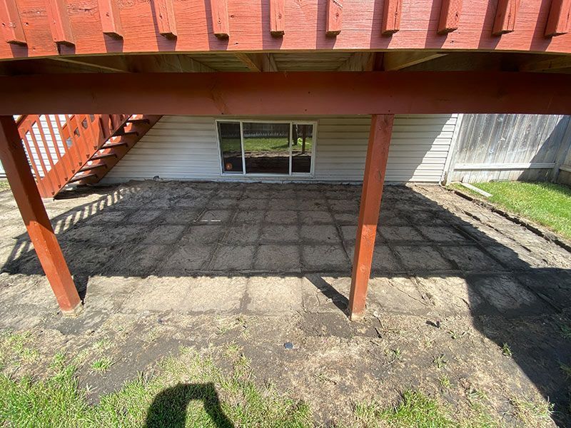 Patio area with red deck above, grass surrounding, and a window on the white house wall.