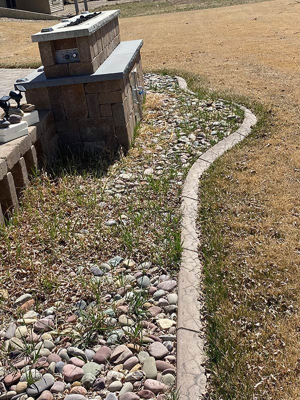 Stone planter and rock bed with a concrete border, surrounded by dry grass.