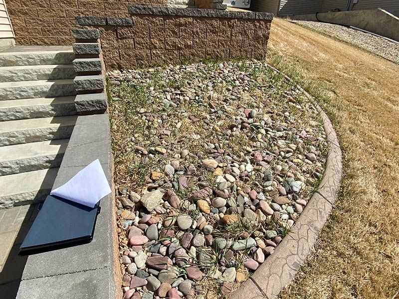 A rock garden with a retaining wall next to stairs. Brown stones and grass, beige borders.