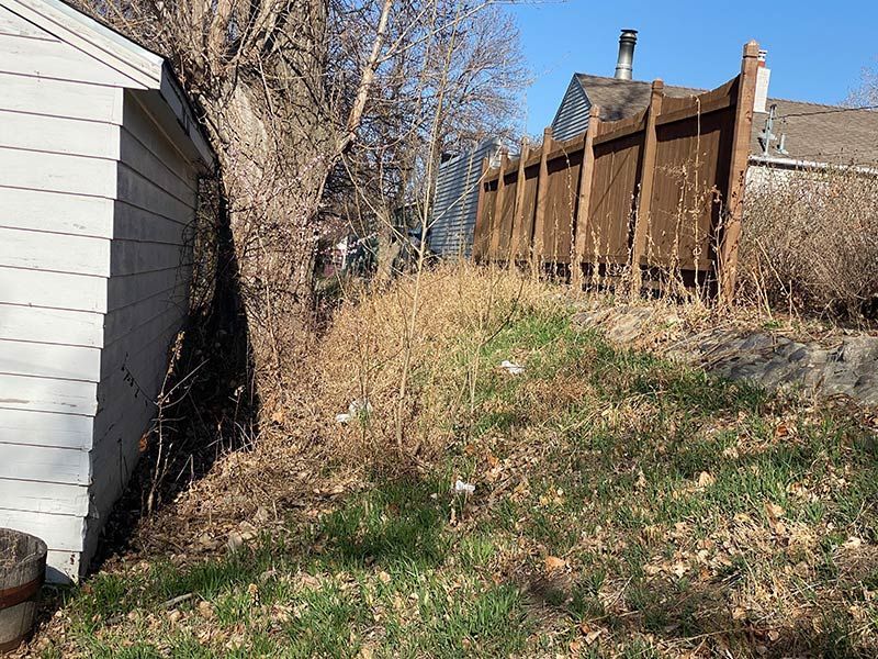 Grassy hill with dry brush, brown wooden fence, and white building in the background on a sunny day.