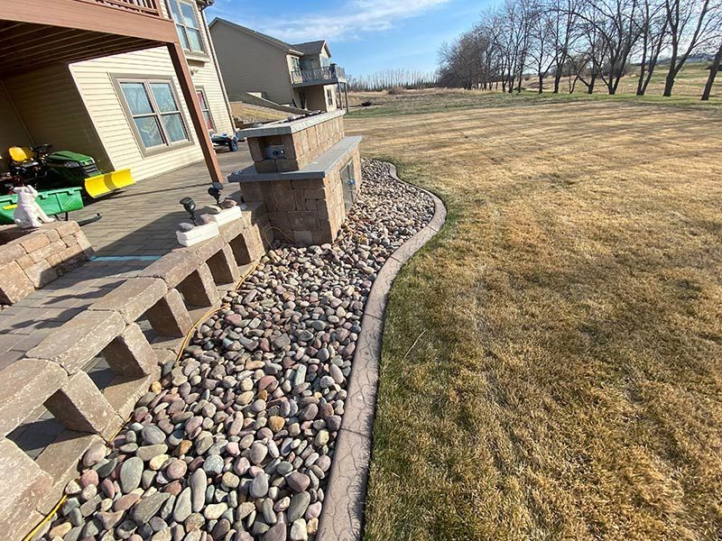 Grassy backyard between two houses, with a dark shadow cast in the foreground and brush in the back.