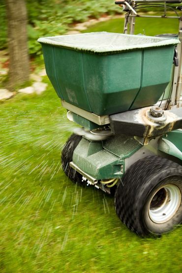 Green lawn spreader dispensing material onto green grass.