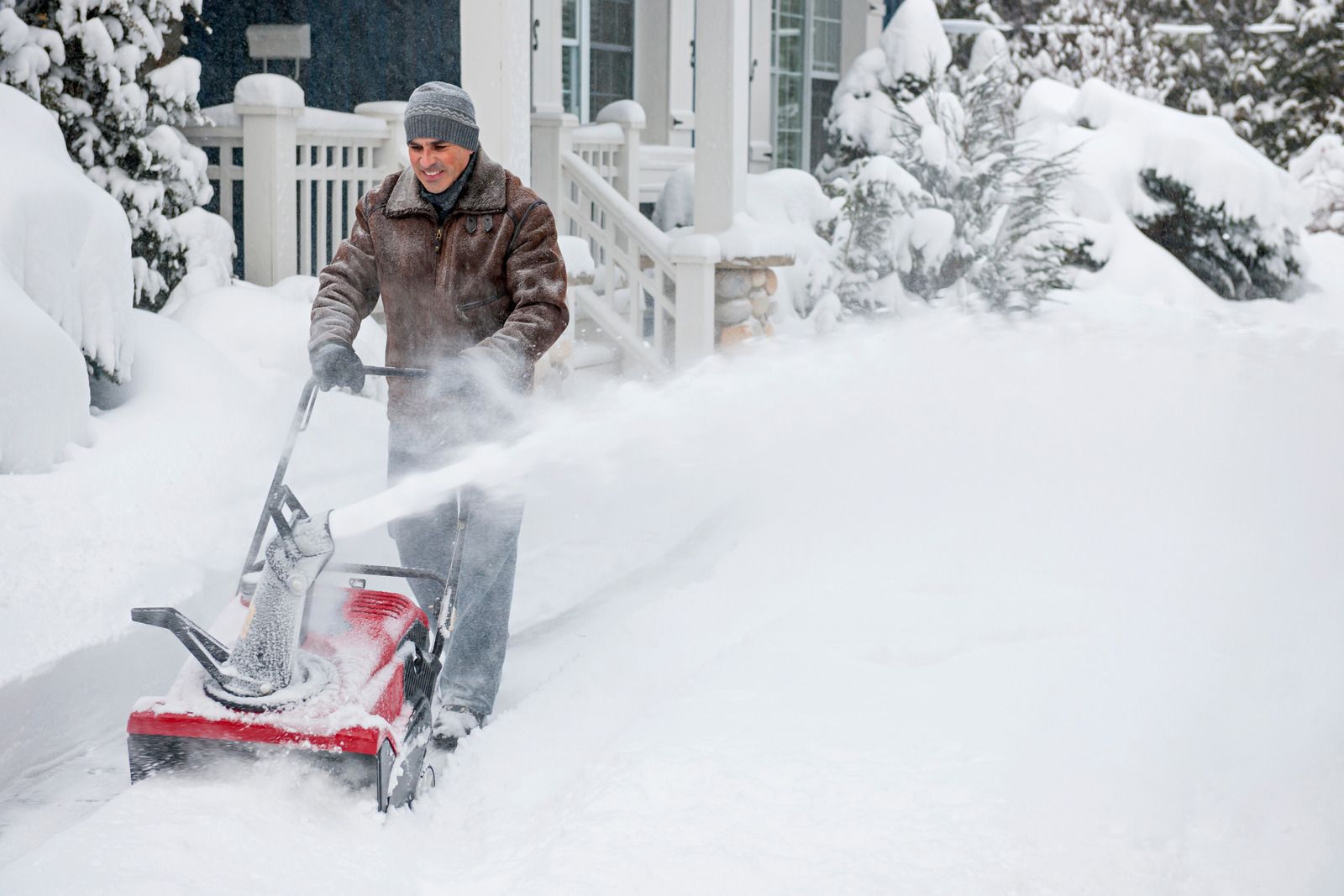 White truck plowing snow from a driveway in front of a brick house on a snowy day.