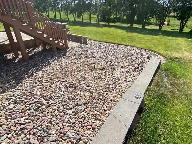 Stone wall and bed of rocks, with grass and concrete edging.