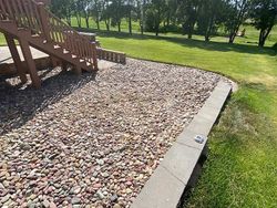 Brown wooden stairs next to a gravel bed, bordered by a low stone wall and green grass.