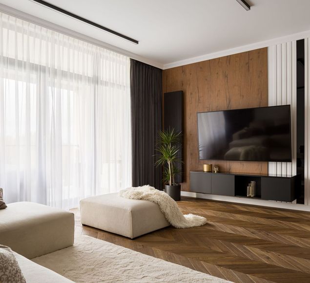 Modern living room with large TV, brown wood accent wall, and large window with sheer curtains.