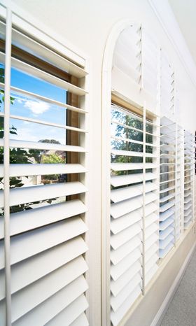 White window shutters, partially open, reveal a sunny sky and trees.