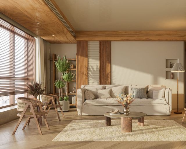 Cozy living room with beige couch, wooden furniture, large windows, and potted plants.