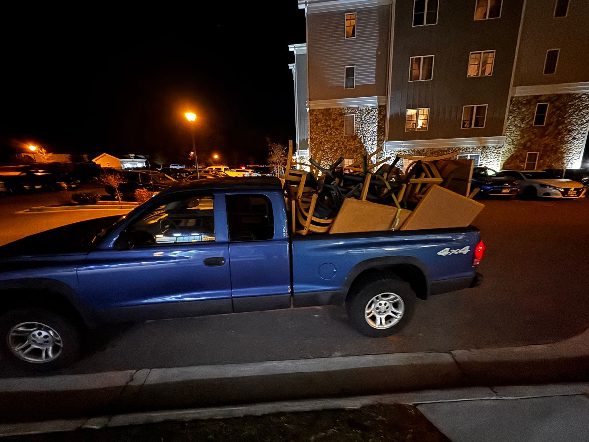 Blue pickup truck loaded with furniture parked near a building at night.
