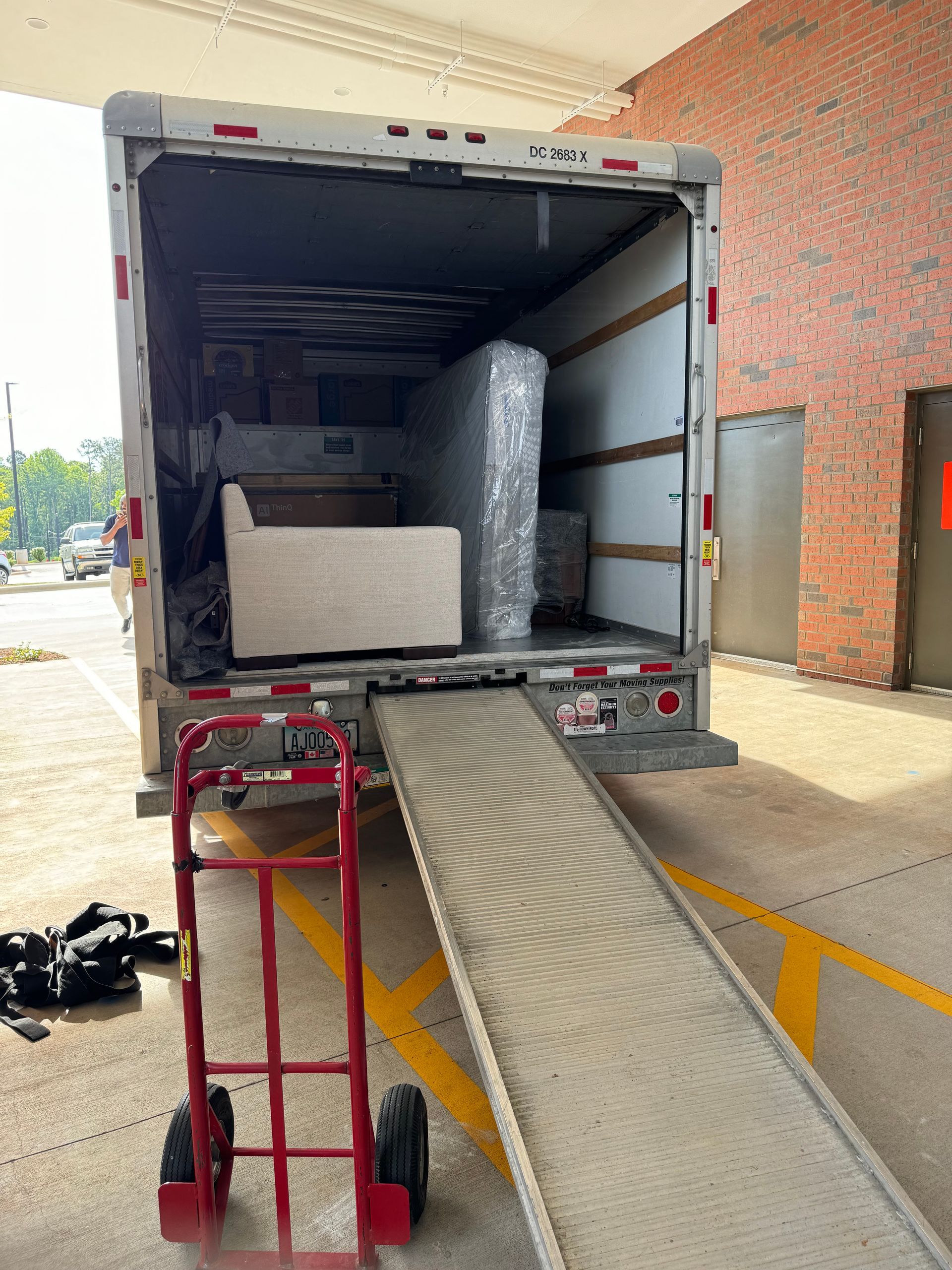 Moving truck loaded with furniture, ramp down. Hand truck in foreground.