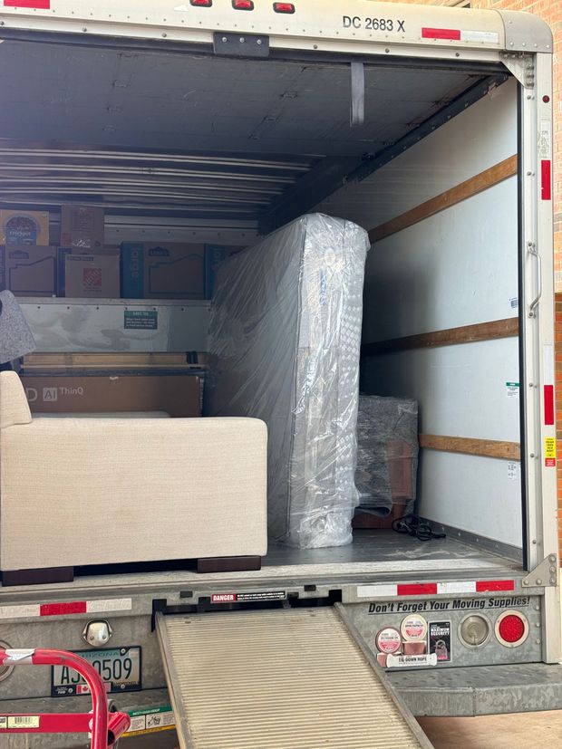 Inside of a moving truck loaded with furniture wrapped in plastic. Boxes are also visible.