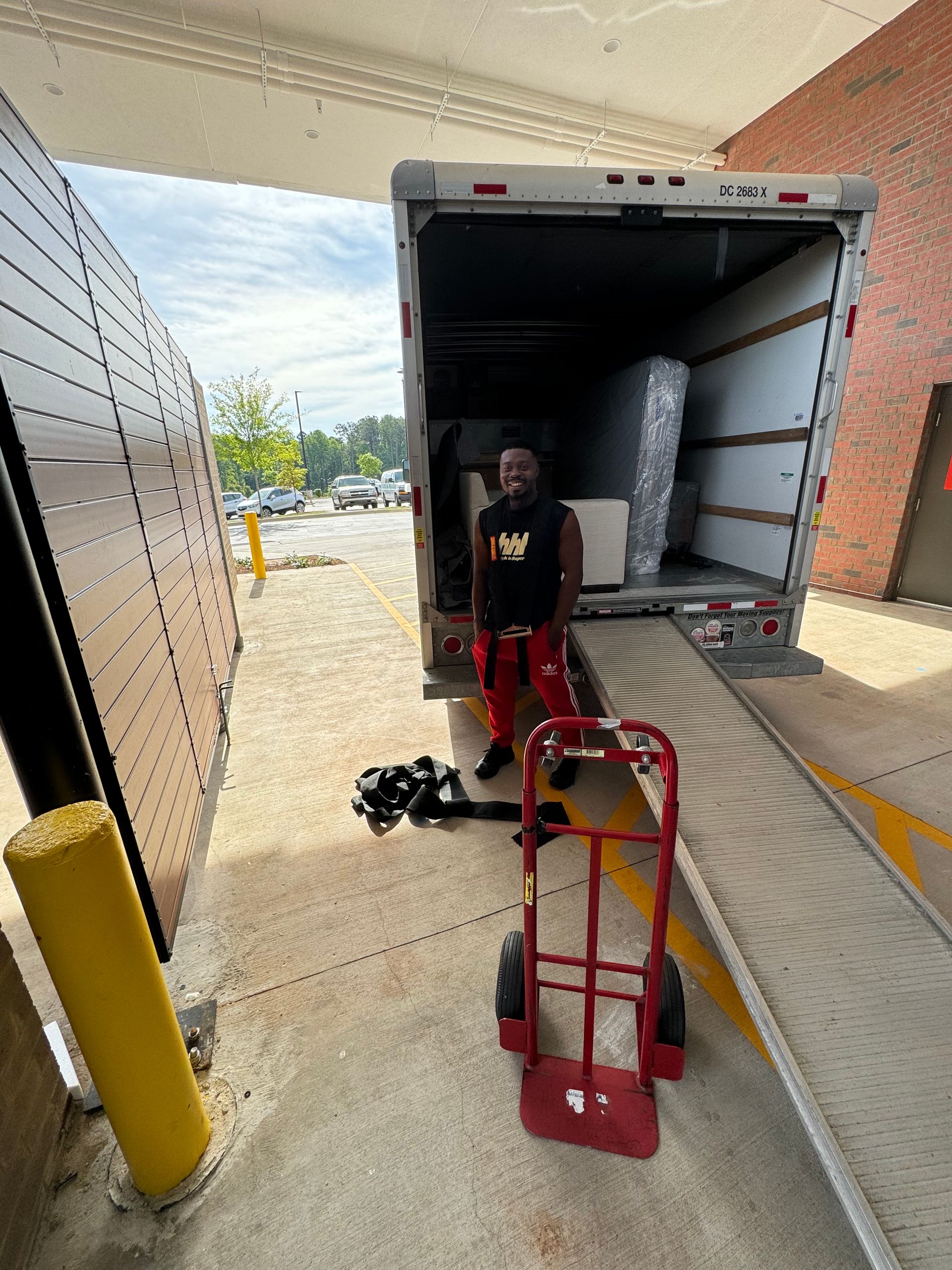 Man loading furniture into a moving truck. He stands in doorway of truck. Hand truck visible.