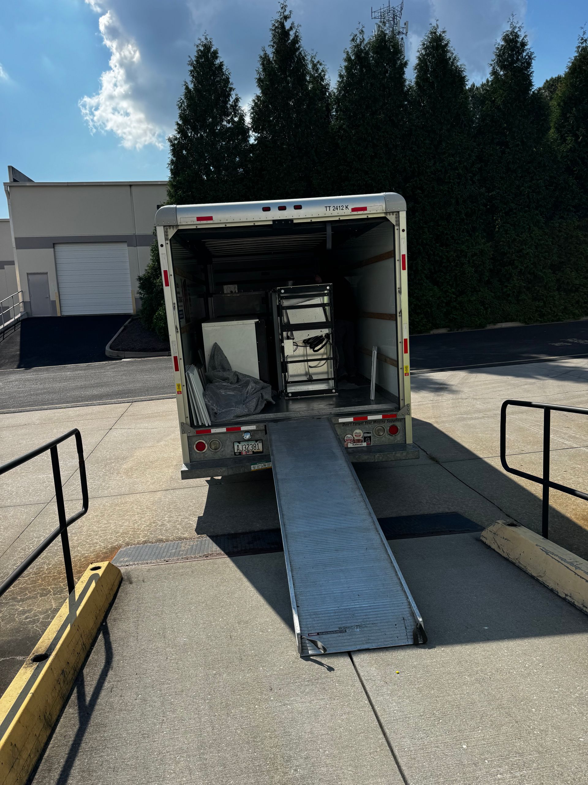 A truck with a ramp lowered, parked at a loading dock, is filled with furniture.