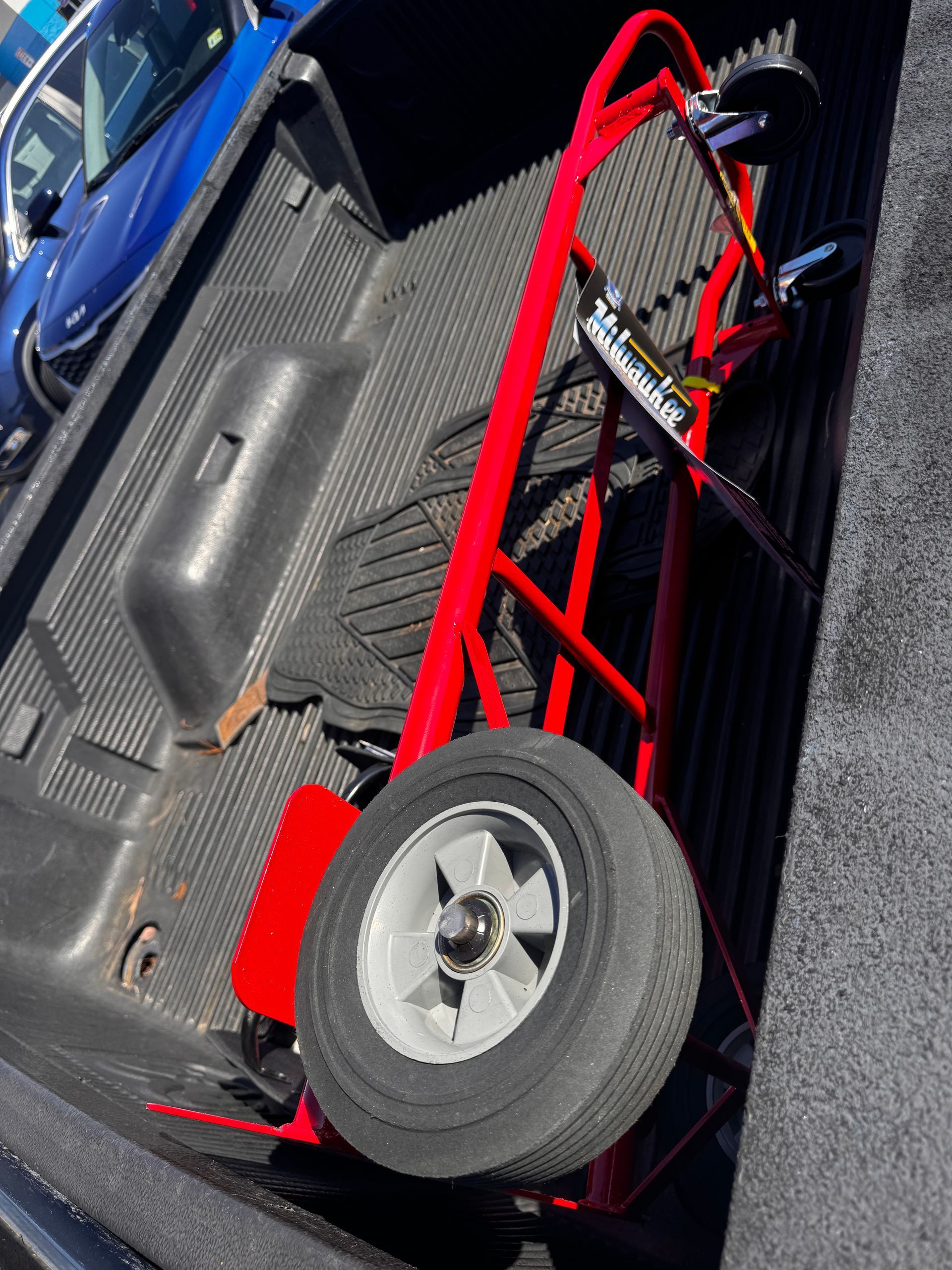 Red hand truck in the bed of a pickup truck with one large wheel.