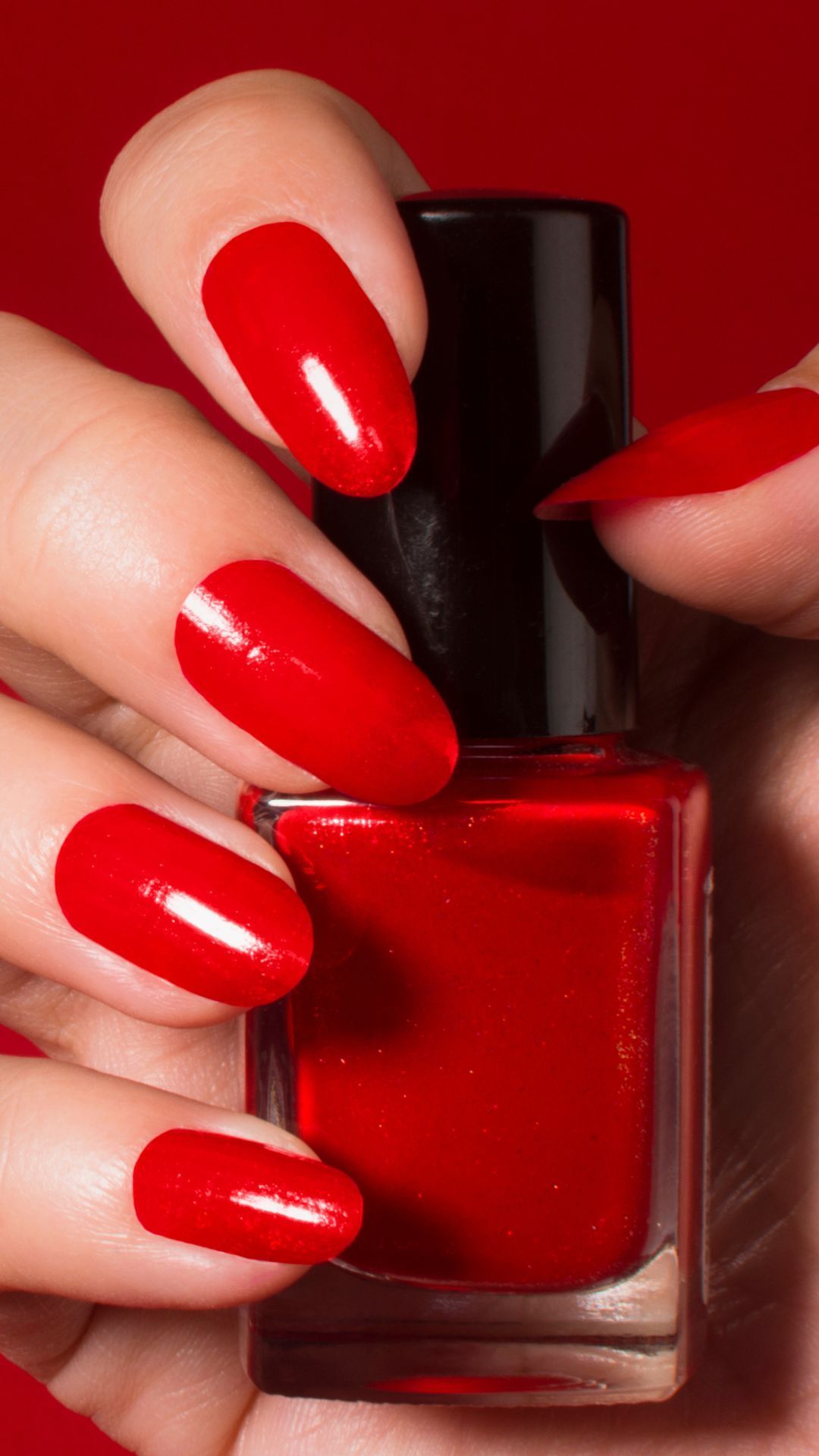 a woman with red nails is holding a bottle of red nail polish .