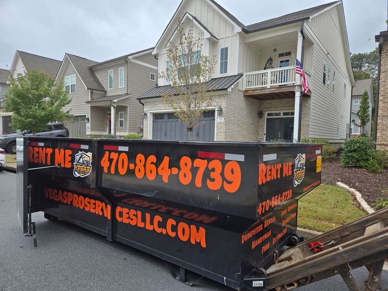 Black dumpster with orange text, in front of a house.