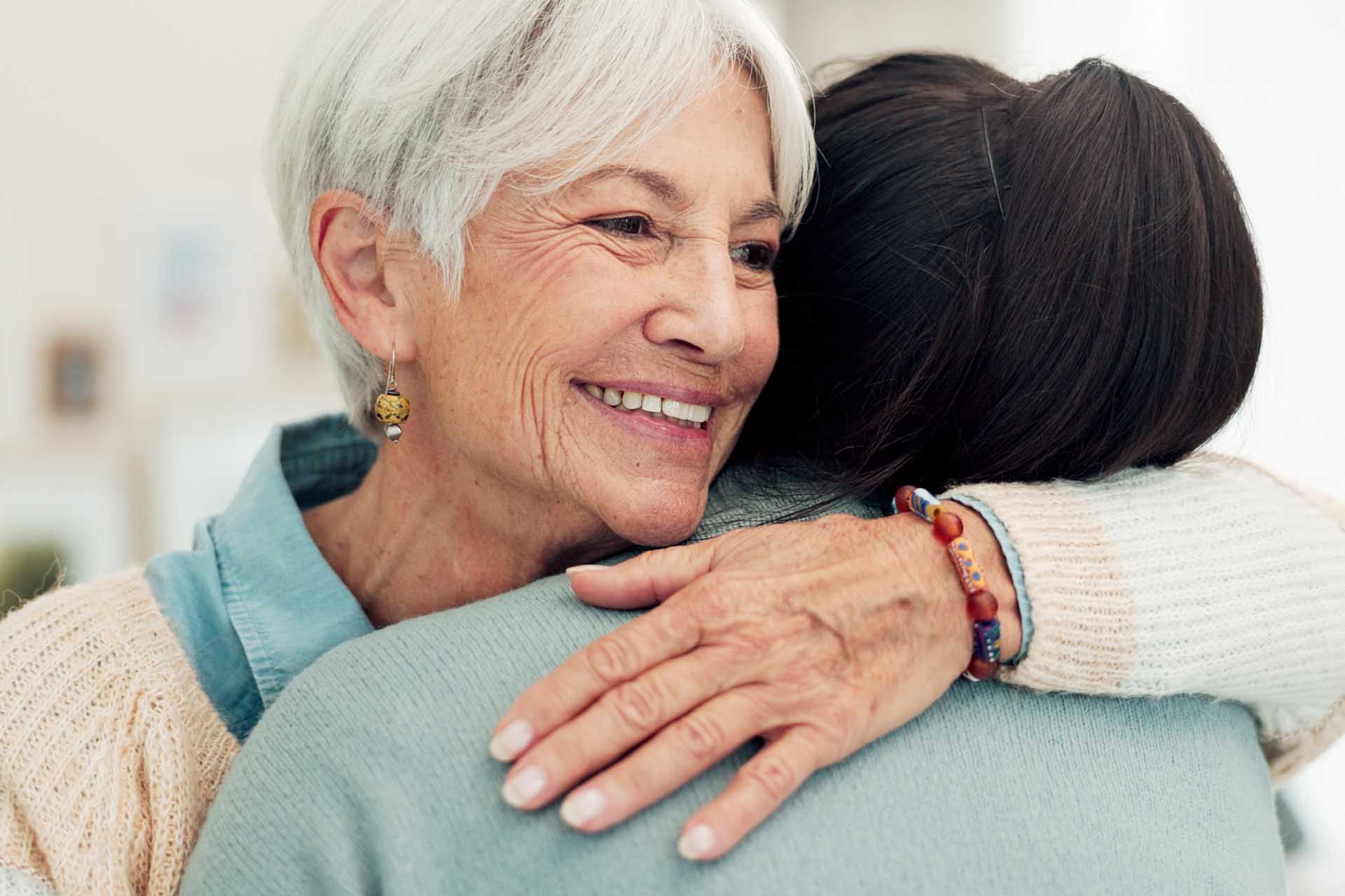 Two people hugging, smiling warmly in a bright indoor setting