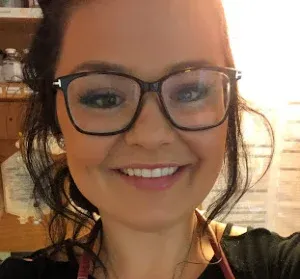 Smiling person wearing glasses indoors, with warm backlighting and a blurred background