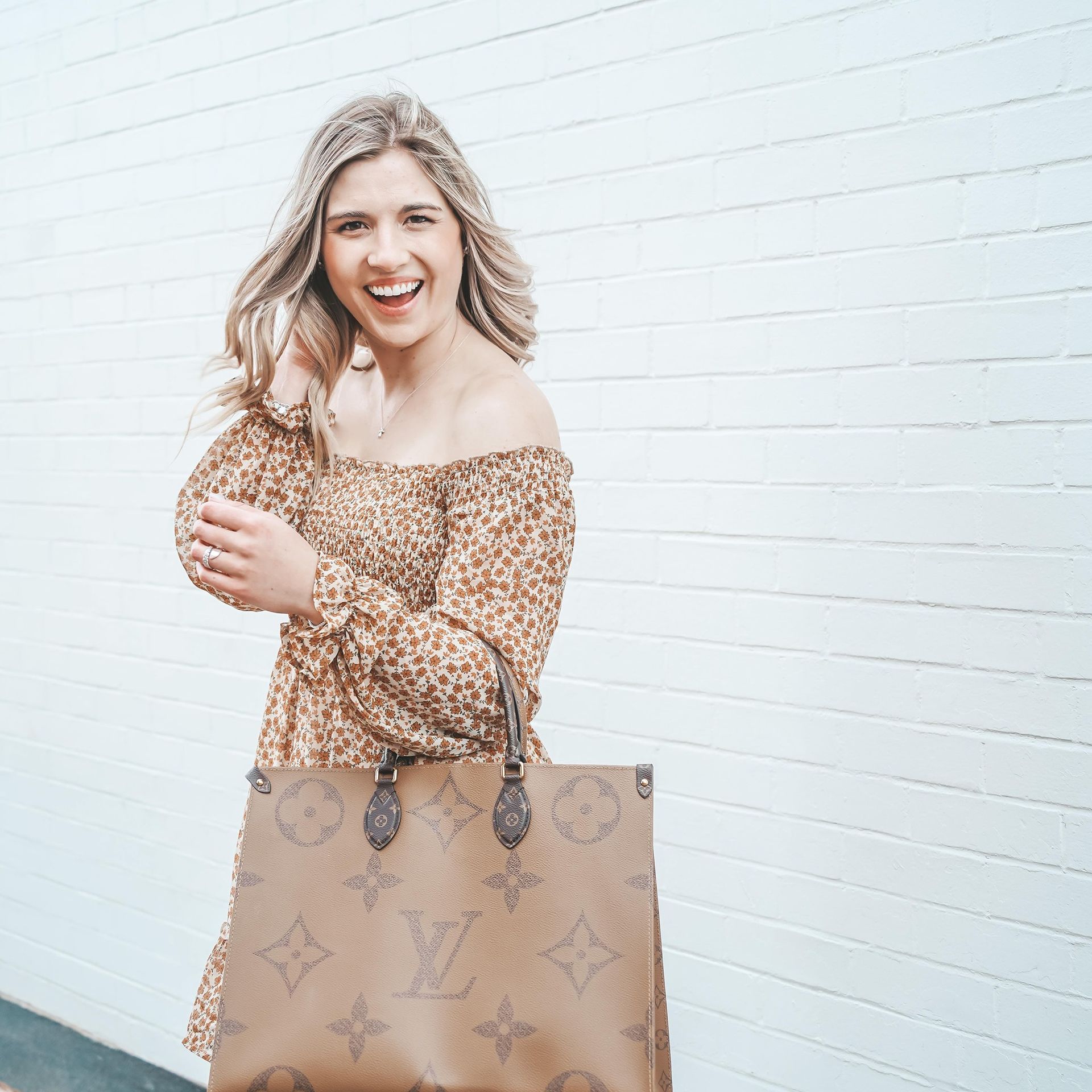 A woman in a leopard print dress is holding a brown louis vuitton bag.