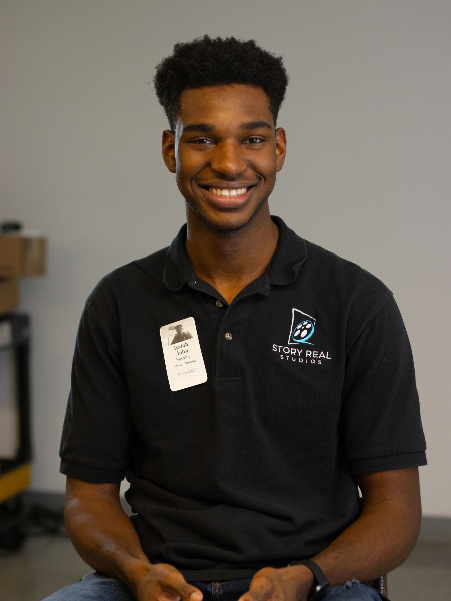 A young man wearing a black polo shirt is smiling for the camera.