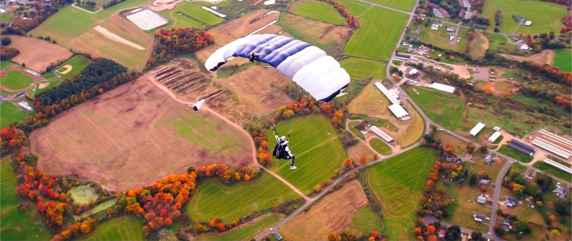 A person is flying through the air with a parachute over a field.