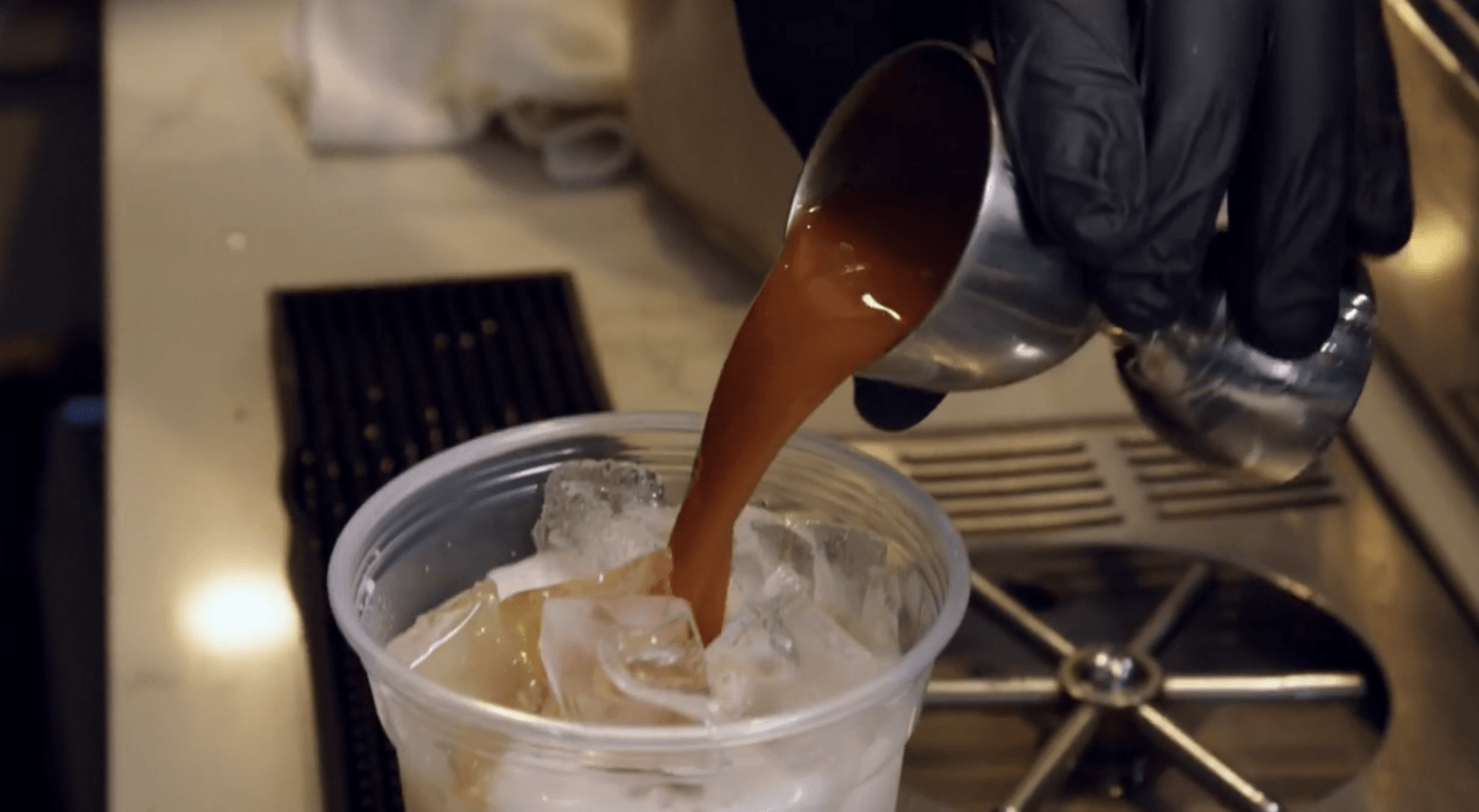 A person is pouring coffee into a plastic cup with ice.