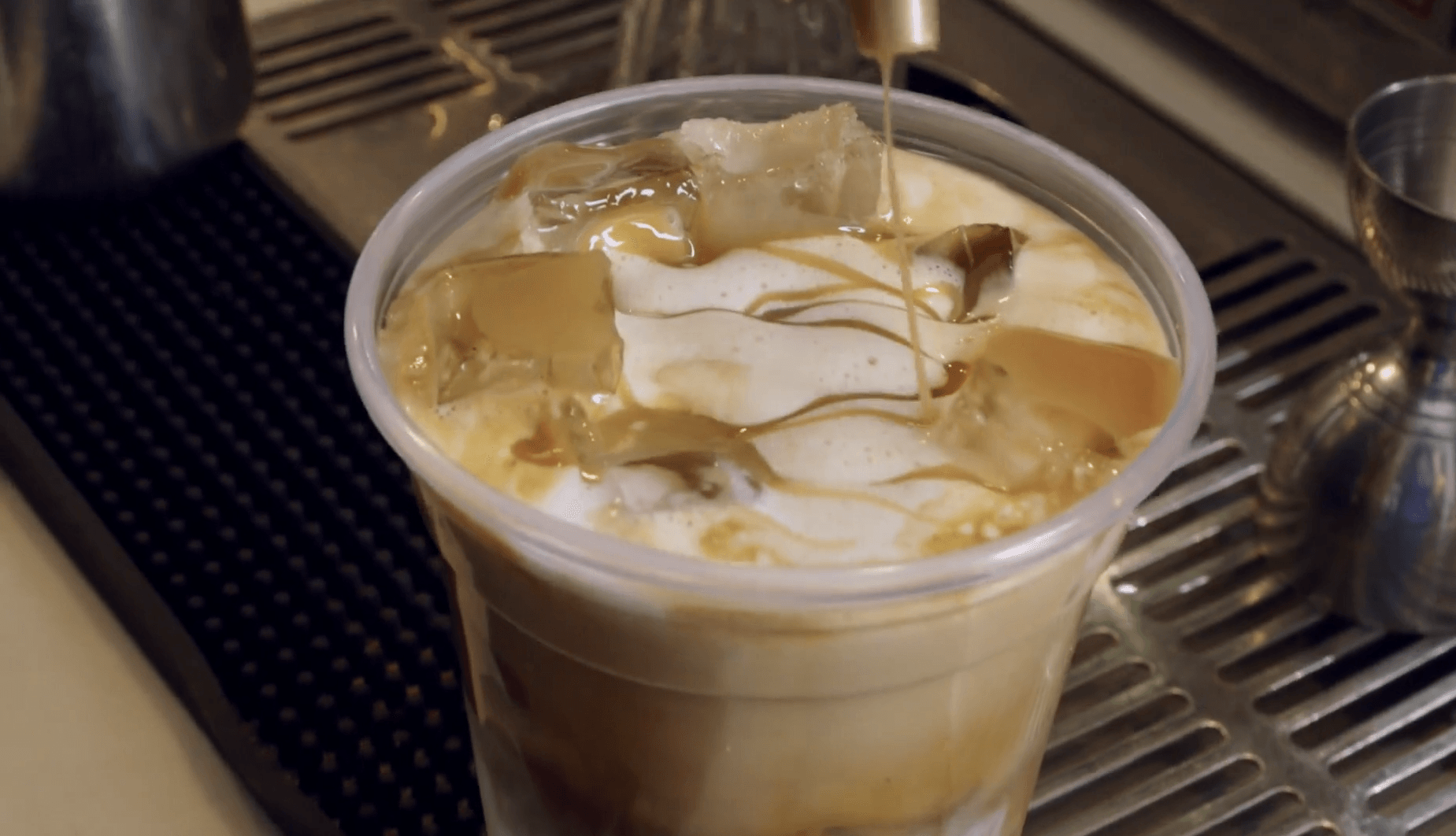 A cup of iced coffee is being poured into a plastic cup.