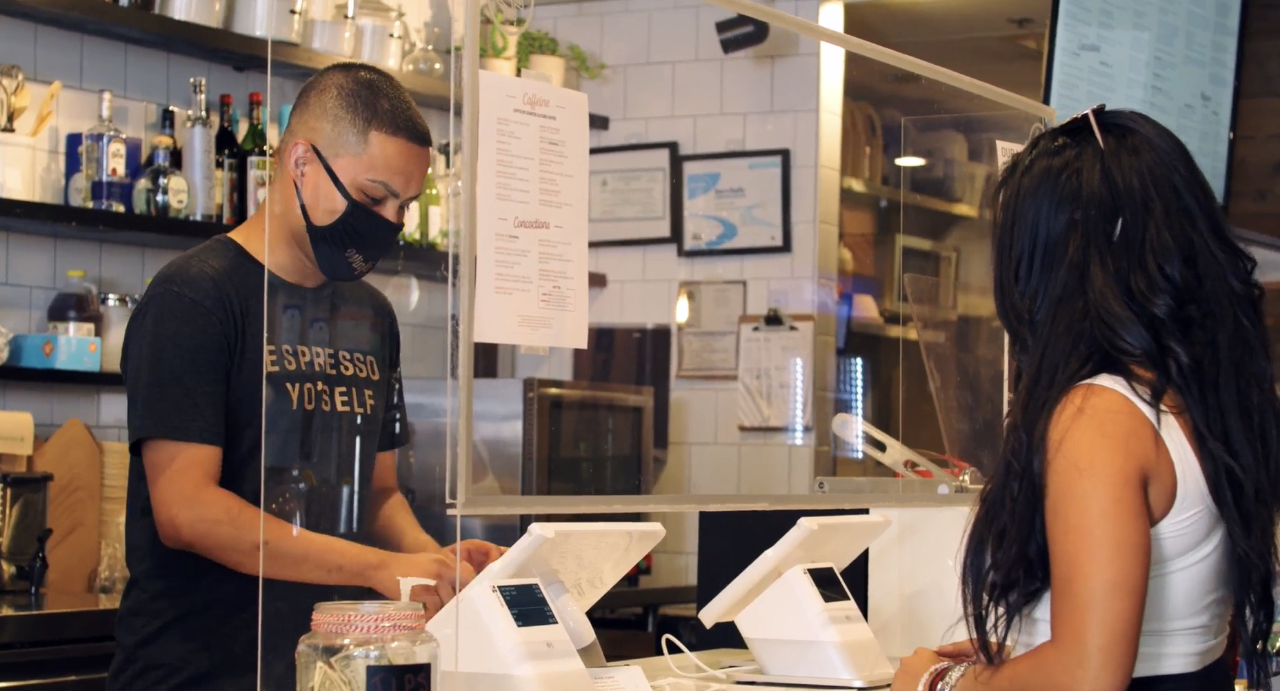 A man wearing a mask is serving a woman in a restaurant.