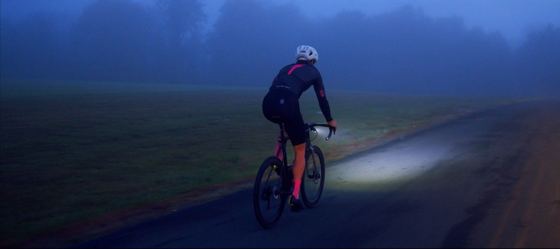 A person is riding a bike on a foggy road at night.