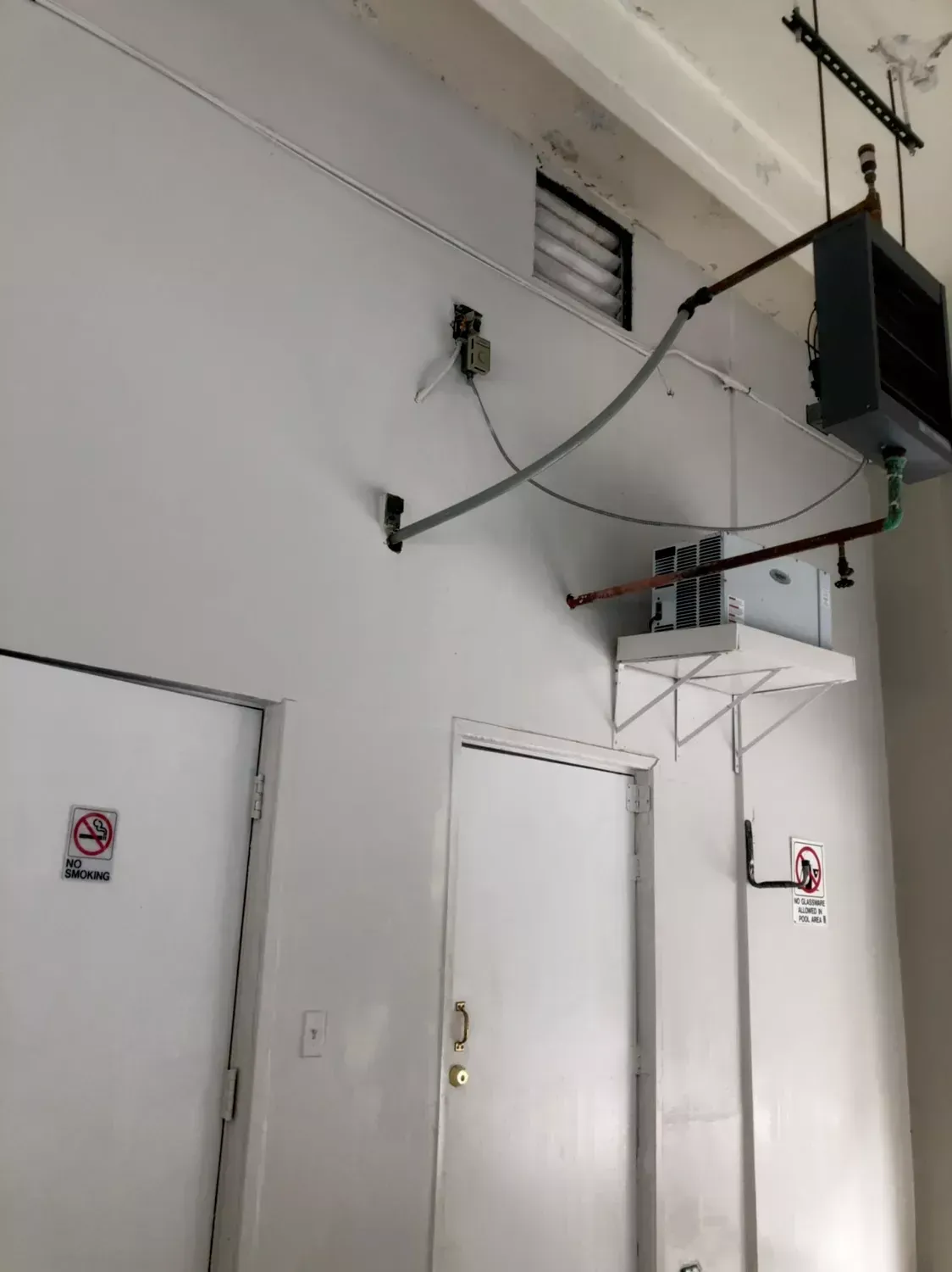 Indoor industrial hallway with white doors, wall-mounted cables, and a suspended equipment platform