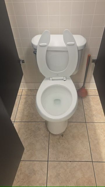 Public restroom toilet with raised seat and grab bars, centered on beige tile floor.