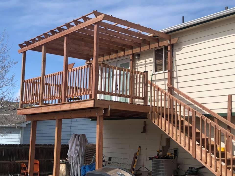 Wooden outdoor deck with pergola roof and staircase attached to a beige house